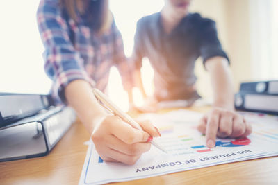 Midsection of business people pointing at graph on table