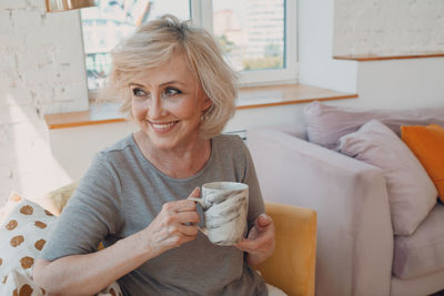 Smiling woman holding mug while sitting at home
