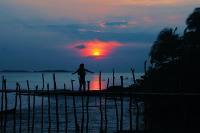 Silhouette man standing by lake against sky during sunset