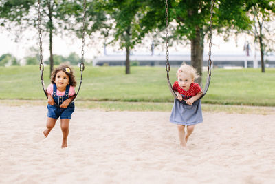 Full length of sisters lying on swings in park