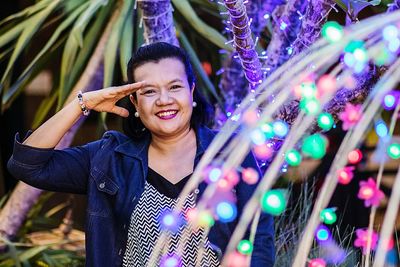 Portrait of smiling woman saluting by illuminated lighting equipment