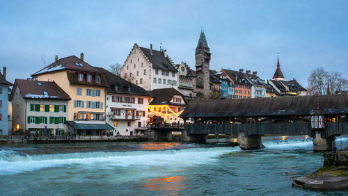 Buildings by river against sky