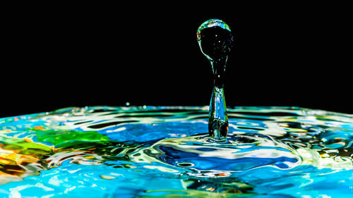 Close-up of drop falling on water against black background