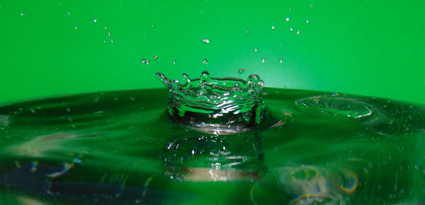 Close-up of drop splashing on water in green container