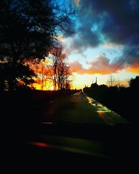 Silhouette trees by road against sky during sunset