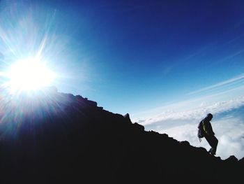 Silhouette man hiking on mountain against bright sun