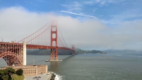 Suspension bridge over river against cloudy sky