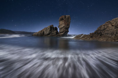 Rock formation in sea against sky at night