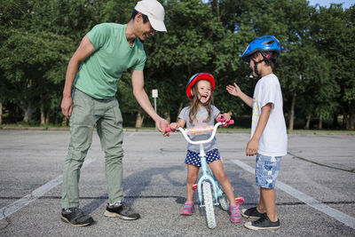 Cheerful girl learning cycling with father and brother at playground