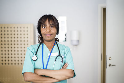 Portrait of mature female healthcare worker with arms crossed standing in clinic