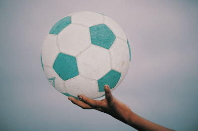 Cropped hand holding ball against sky