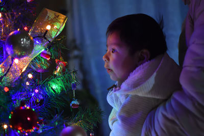 Midsection of mother carrying cute son looking at illuminated christmas tree