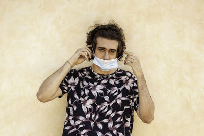 Portrait of young man wearing mask standing against wall