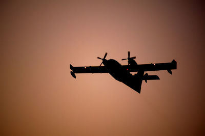 Low angle view of silhouette airplane against clear sky during sunset