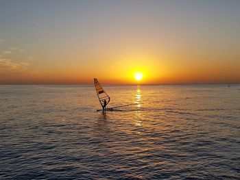 Silhouette person in sea against sky during sunset