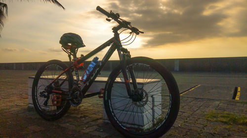 Bicycle on beach against sky during sunset