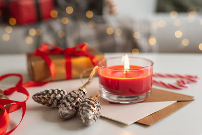 View of a bright red candle, christmas gift, and postcards against a garland lights background.