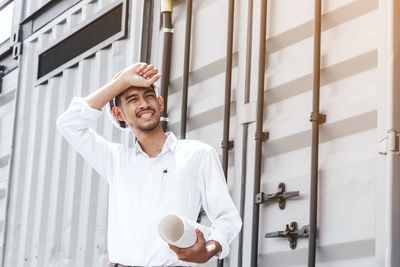 Tired engineer wearing hardhat standing at construction site during sunny day