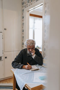 Senior man with hand on chin solving soduko puzzle while sitting at home