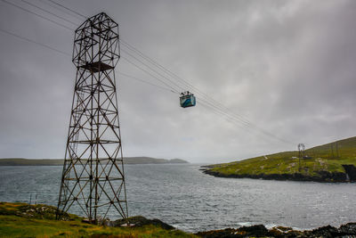 Low angle view of overhead cable car over sea against cloudy sky
