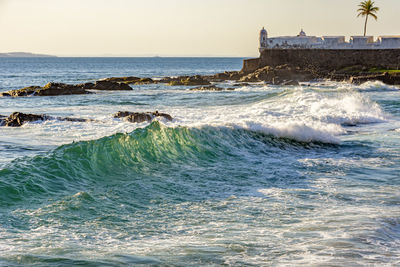 Salvador sea waves with an old colonial fortress from the empire era in background during sunset.