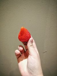 Midsection of person holding strawberry against wall