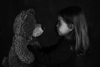 Close-up of girl with toy against black background