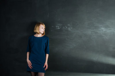 Young woman standing against gray wall