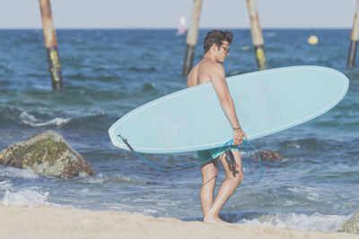 Shirtless man carrying surfboard at beach