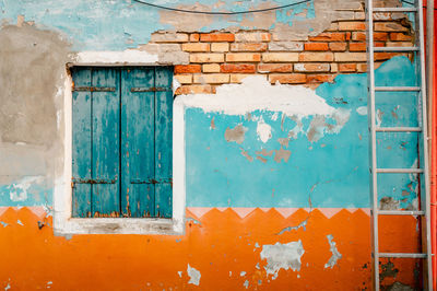 Ancient facade of dwelling with ruined orange and blue plaster