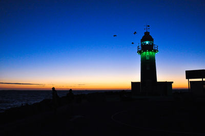 Silhouette lighthouse by sea against clear sky during sunset