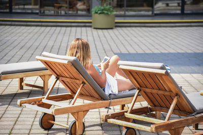 Young woman using mobile phone while sitting on deck chair