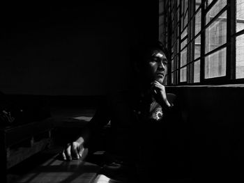 Young man looking through window while sitting in darkroom