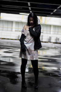 Full length of young woman standing on wet floor in parking lot