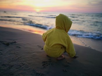 Boy crouching at sea shore