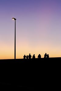 Silhouette people on street against orange sky