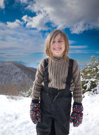 Portrait of young woman standing on snow covered field against sky