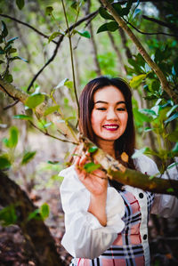 Portrait of smiling young woman standing against plants