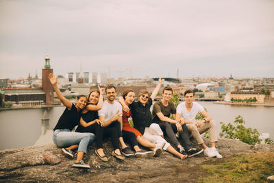 Portrait of happy friends sitting on rock formation against sky