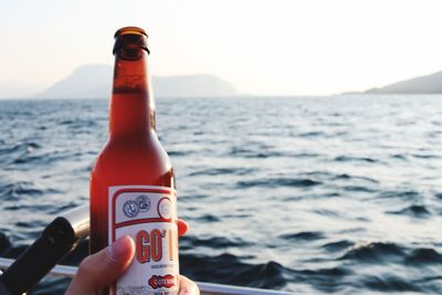 Person holding bottle by sea against sky