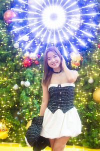 Young woman standing by christmas tree at night