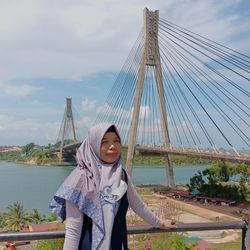 Portrait of smiling young woman standing against bridge