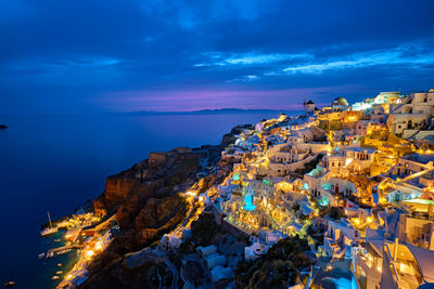 High angle view of illuminated city by sea against sky