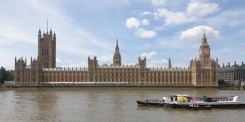 Buildings by river against cloudy sky