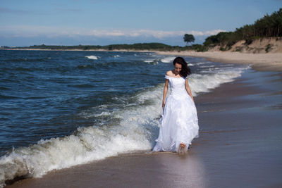 Full length of bride walking on shore at beach against sky