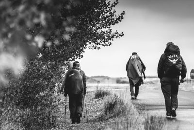 Rear view of people walking on field against sky