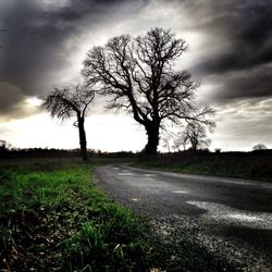 Road passing through field against cloudy sky