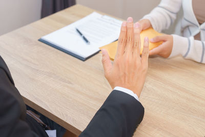 Cropped hand of businessman showing stop gesture to female colleague giving currency in office