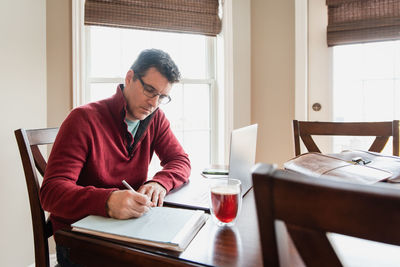 Man in glasses working from home using a computer at a dining table.