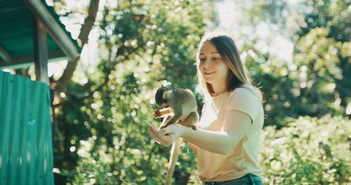 Young woman standing by plants against trees